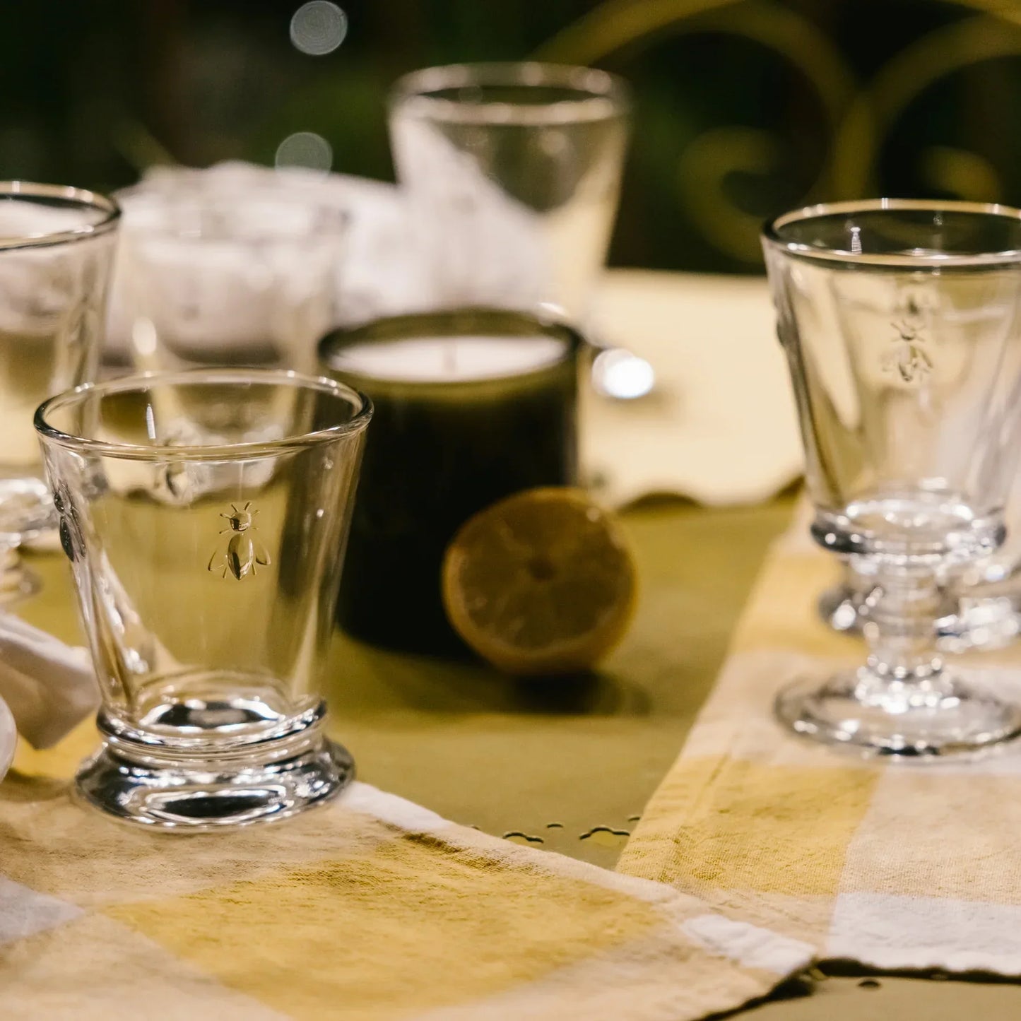 Clear glass cups with bee motifs on a yellow and white striped tablecloth, lemon and candle background