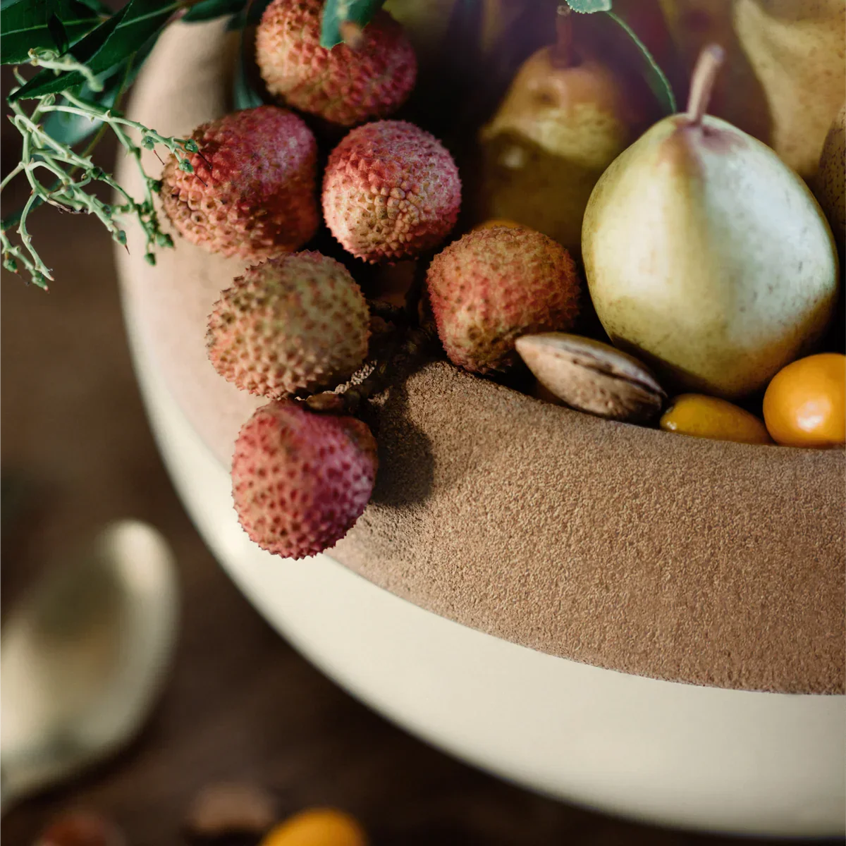 Close-up of a beige clay large storage bowl filled with lychee, pears, nuts, and small orange fruits