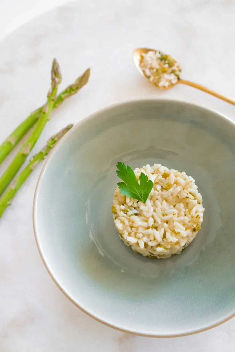 Creamy risotto with asparagus and leeks garnished with a parsley leaf on a gray plate