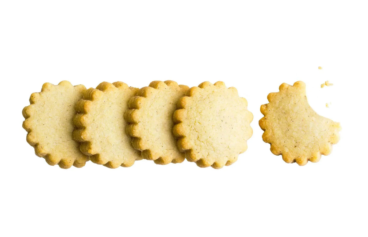 Five scalloped edge butter cookies in a row on white background, one with a bite taken