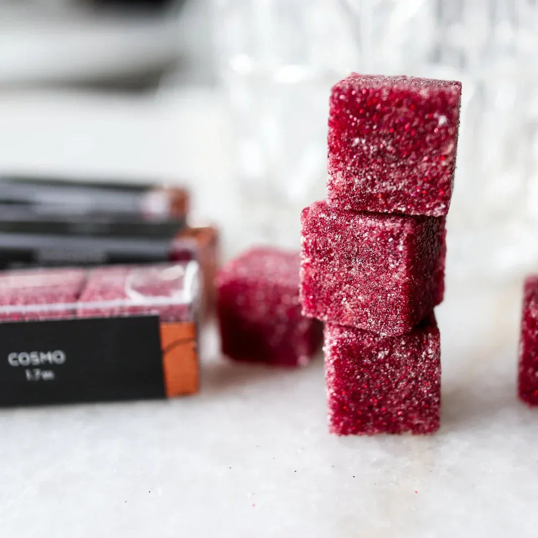 Stack of three red Cosmo sugar cubes coated with granulated sugar on white surface with packaging in background
