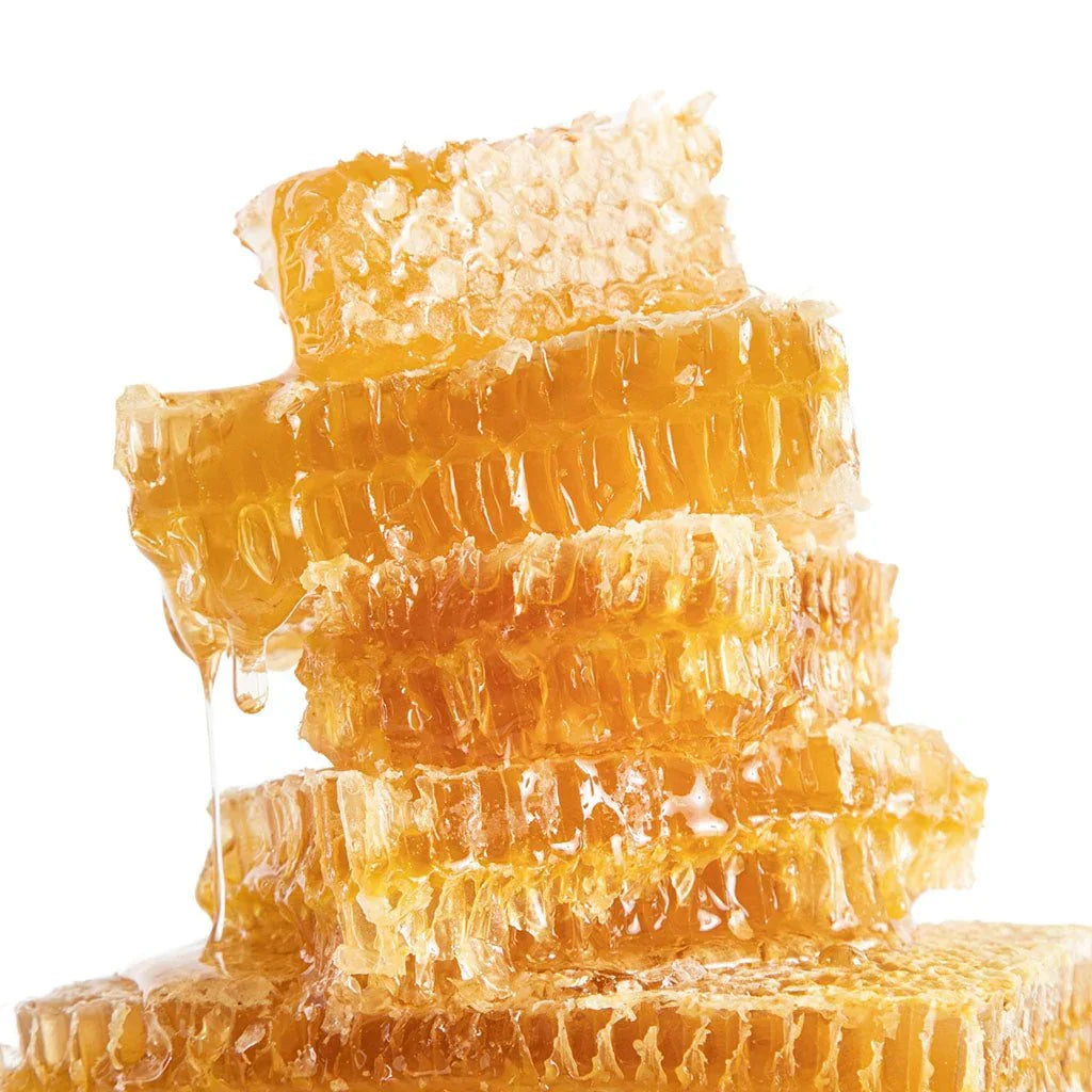 Close-up of golden honeycomb pieces stacked with honey dripping, isolated on white background