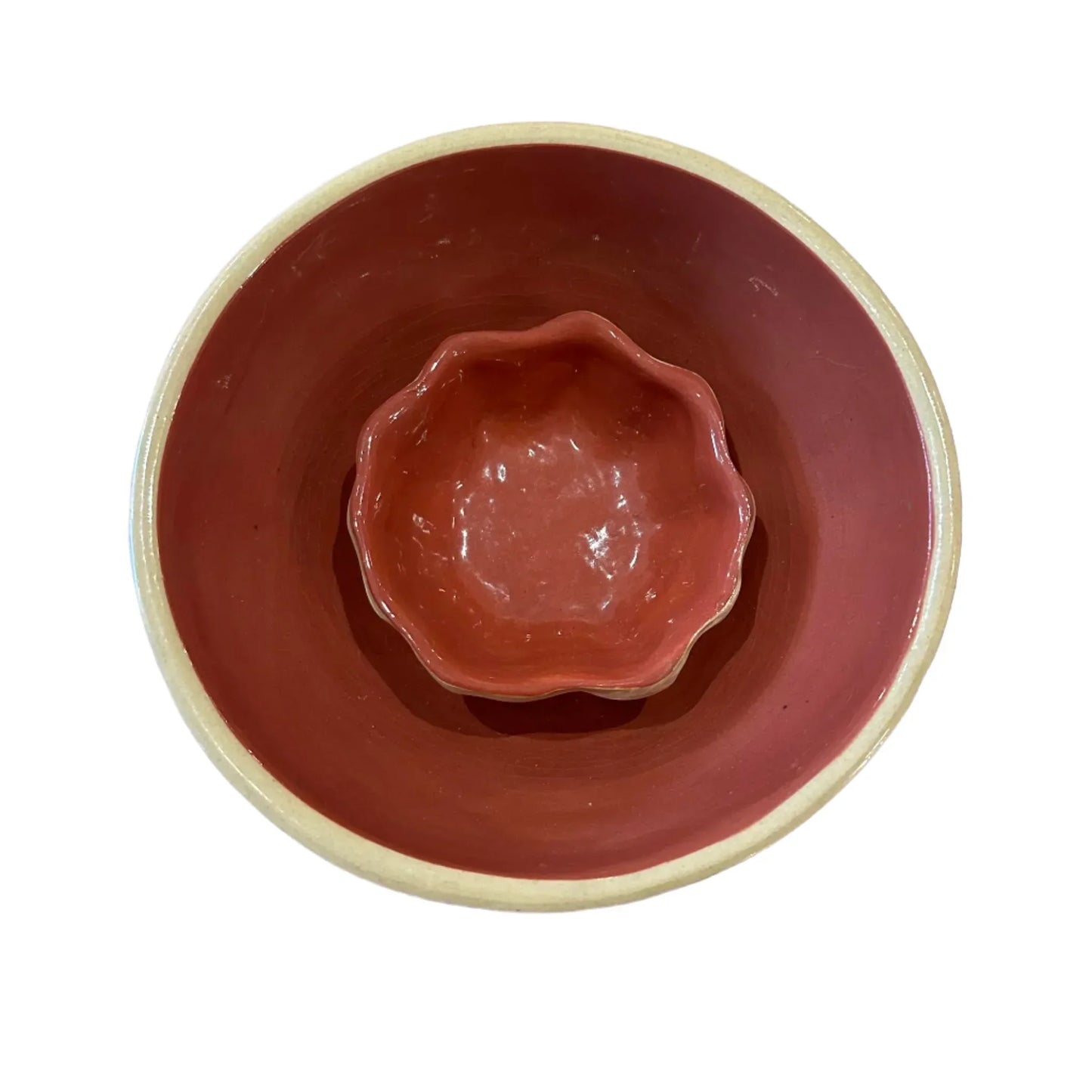 Red ceramic bowl with a smaller decorative bowl inside on a textured surface