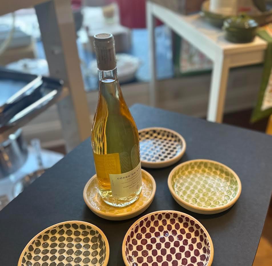 Bottle of white wine on a yellow and white polka dot ceramic coaster, surrounded by four colorful polka dot coasters on a black table