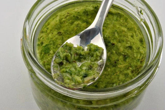 Close-up of green herb pesto sauce in a glass jar with a spoon scooping some out