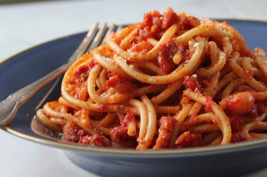 Bucatini pasta with amatriciana sauce, garnished with grated cheese, served in a blue bowl with a fork