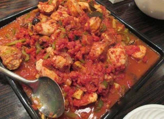 Plate of chicken cacciatore with tomato sauce, green peppers, olives, and served with a spoon