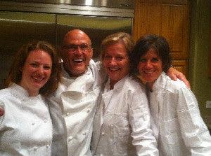 Four chefs in white uniforms posing and smiling together in a professional kitchen