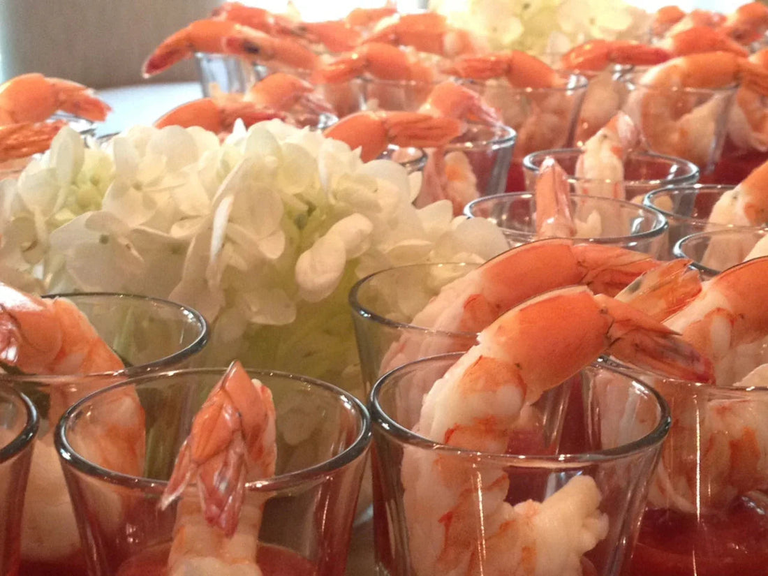 Shrimp cocktail appetizers served in clear glasses with white flowers in the background