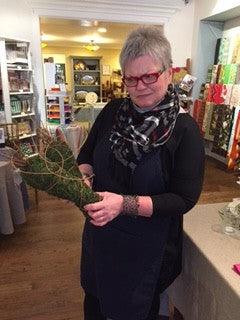 Woman with short gray hair and red glasses arranging a green potted plant inside a cozy flower shop
