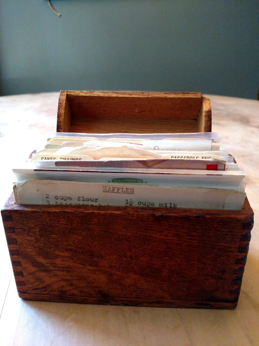 Vintage wooden recipe box filled with worn, typed recipe cards on kitchen table