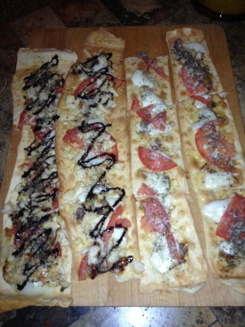 Four rectangular flatbread pizzas topped with cheese, tomato slices, herbs, and balsamic glaze on a wooden cutting board