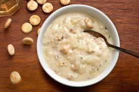 Bowl of creamy clam chowder with spoon, crackers on wooden table