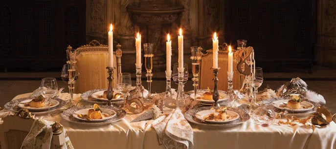 Elegant dining table set with lit candles, gold accents, masks, and fine china in a dim room