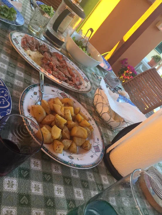 Dinner table with roasted potatoes, sliced meat, salad bowl, and drinks on a green checkered tablecloth