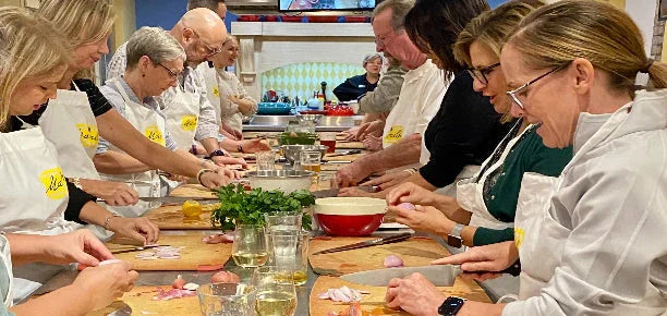 Group of adults wearing aprons chopping vegetables together in a cooking class kitchen