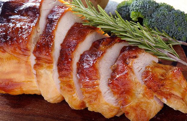Sliced roasted turkey breast with golden brown skin, garnished with fresh rosemary and broccoli florets