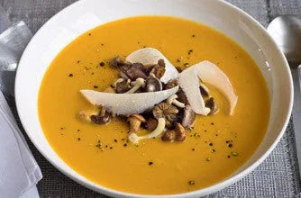Creamy pumpkin soup garnished with mushroom slices, nuts, and herbs in a white bowl