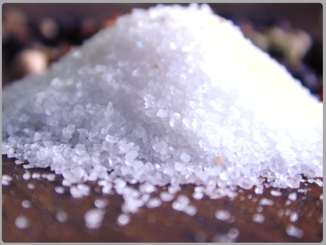 Close-up of coarse white sea salt crystals piled on a wooden surface