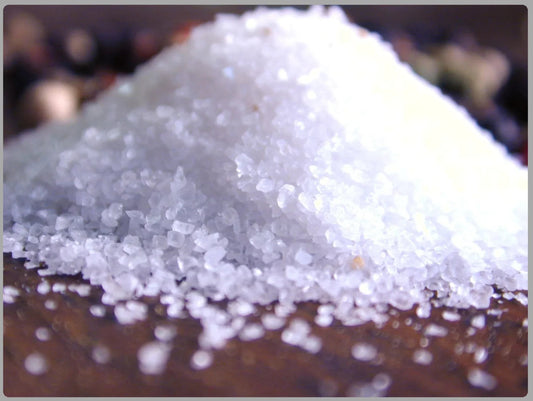 Close-up of coarse white sea salt crystals piled on a wooden surface
