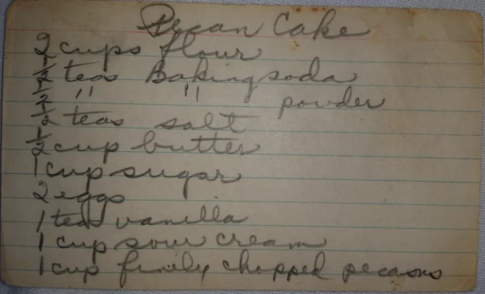 Handwritten vintage recipe card for pecan cake with ingredients like flour, baking soda, butter, sugar, eggs, vanilla, sour cream, and pecans