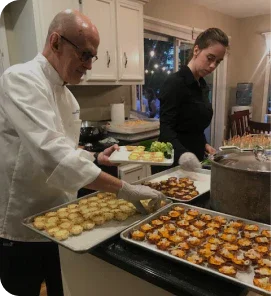 Chefs preparing and plating a variety of appetizers in a kitchen setting with trays of hors d'oeuvres