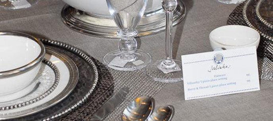 Elegant table setting with fine china, silver-rimmed plates, crystal glassware, and a gift registry card