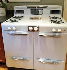 Vintage white gas stove with chrome handles and four burners in a kitchen setting