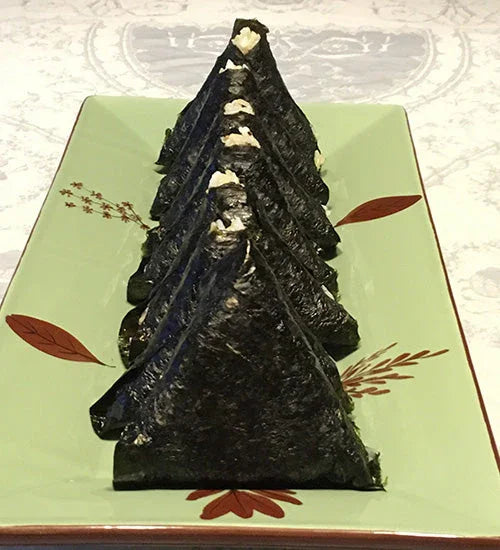 Row of triangular sushi wrapped in dark seaweed on a green rectangular plate with leaf designs