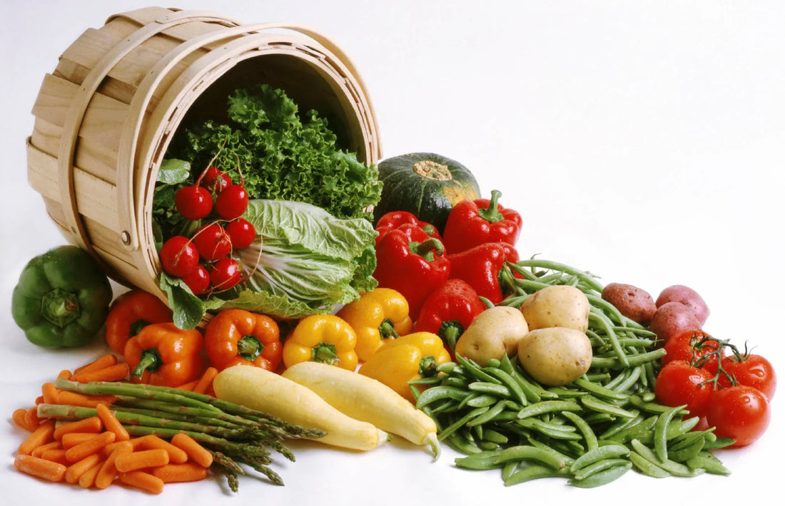 Wooden basket spilling fresh vegetables including lettuce, cherry tomatoes, bell peppers, green beans, potatoes, squash, carrots, asparagus, and tomatoes