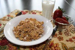 Bowl of cereal flakes with milk and fresh strawberries on a floral tablecloth