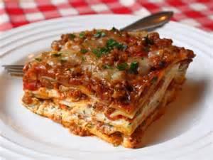 Close-up of a layered slice of homemade lasagna on a white plate with red checkered tablecloth
