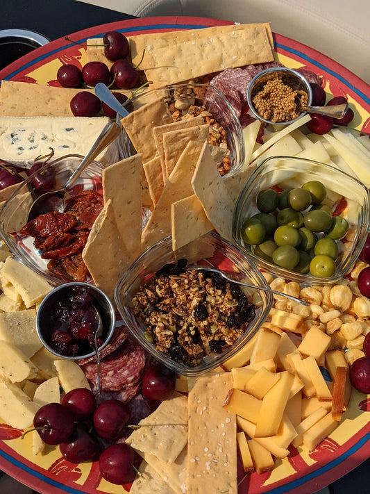 Colorful charcuterie board with various cheeses, green olives, crackers, dried fruits, mustard, salami, and fresh cherries