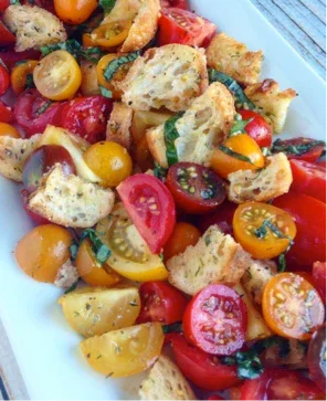 Close-up of colorful panzanella salad with cherry tomatoes, toasted bread, and fresh basil on white plate