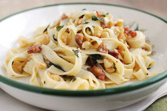Close-up of creamy pasta carbonara with bacon and herbs in a white bowl with green rim