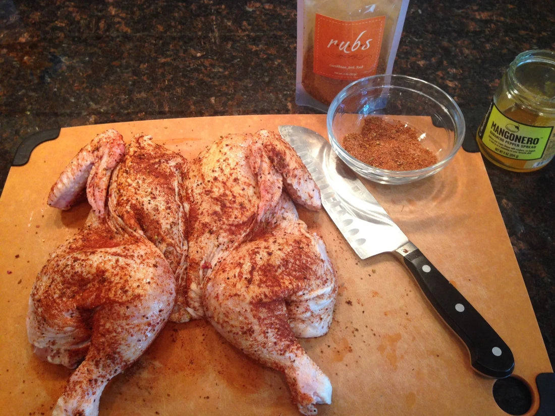 Whole spatchcocked chicken seasoned with Caribbean jerk rub on cutting board with chef knife and habanero pepper spread
