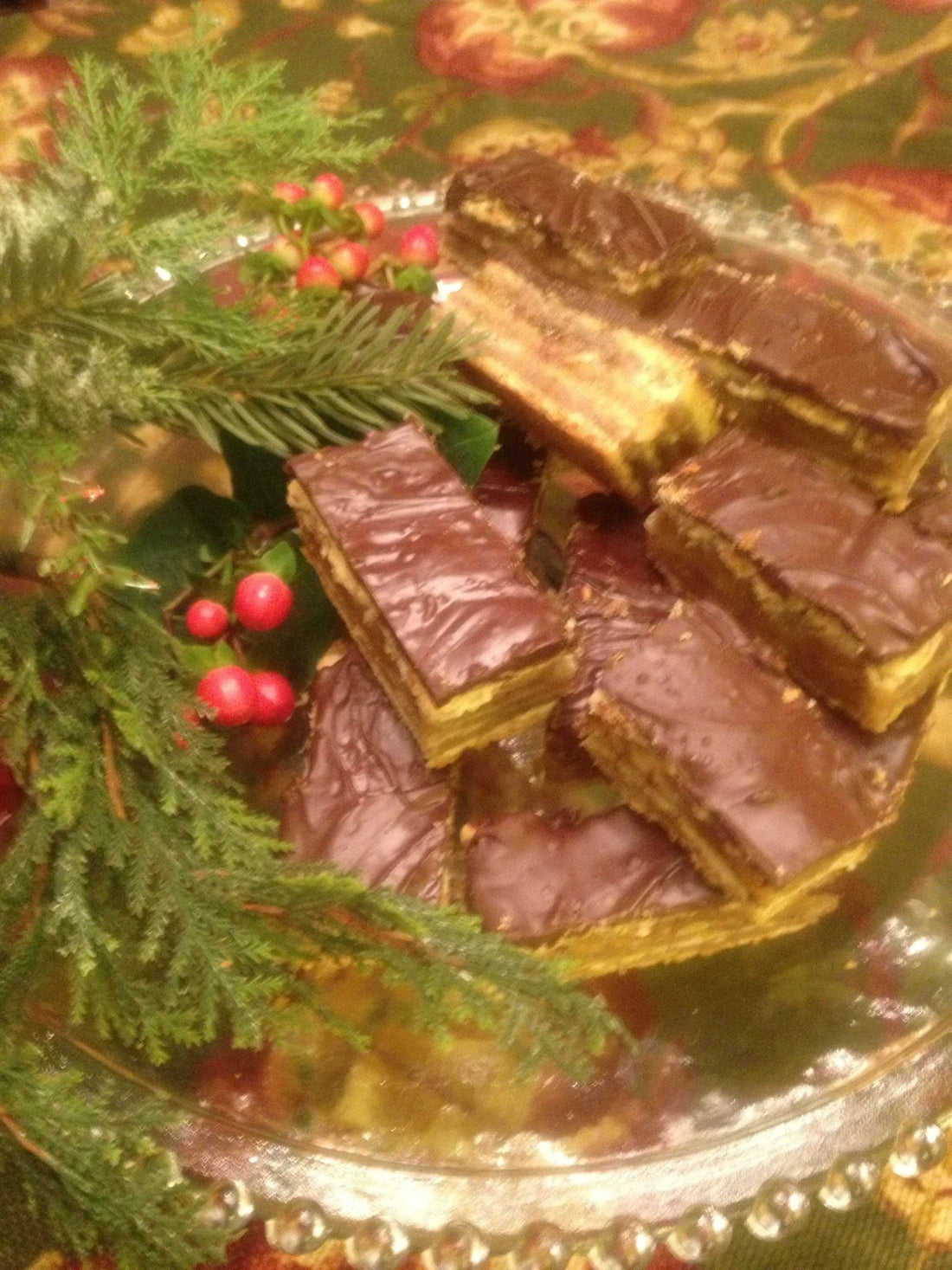 Chocolate-covered layered wafer cookies on glass plate with festive greenery and red berries