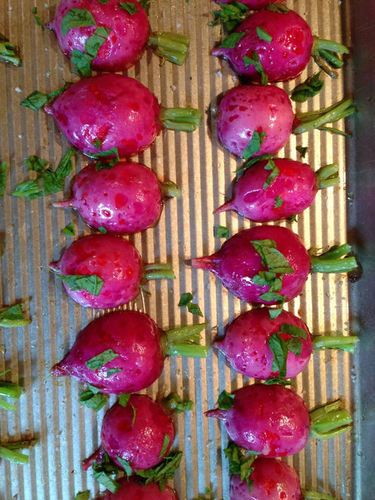 Fresh red radishes with green tops on a ribbed metal baking sheet sprinkled with chopped herbs