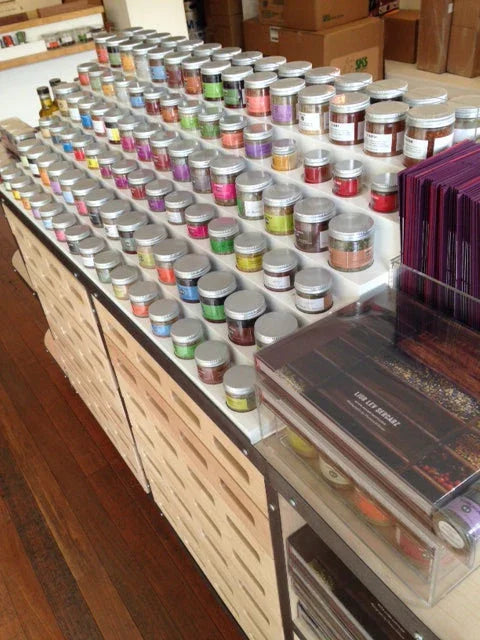 Rows of colorful spice jars with silver lids neatly arranged on a display table in a store