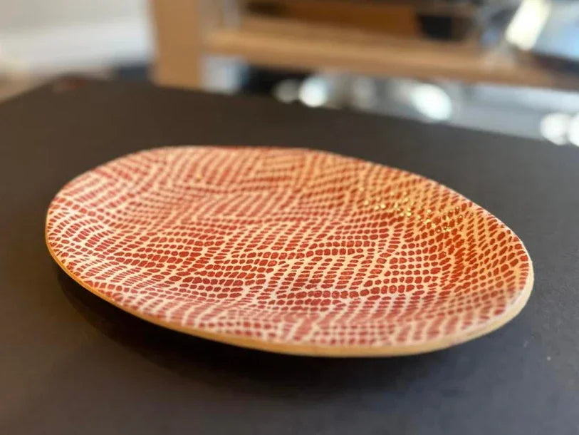 Round decorative plate with red and white textured pattern on black surface