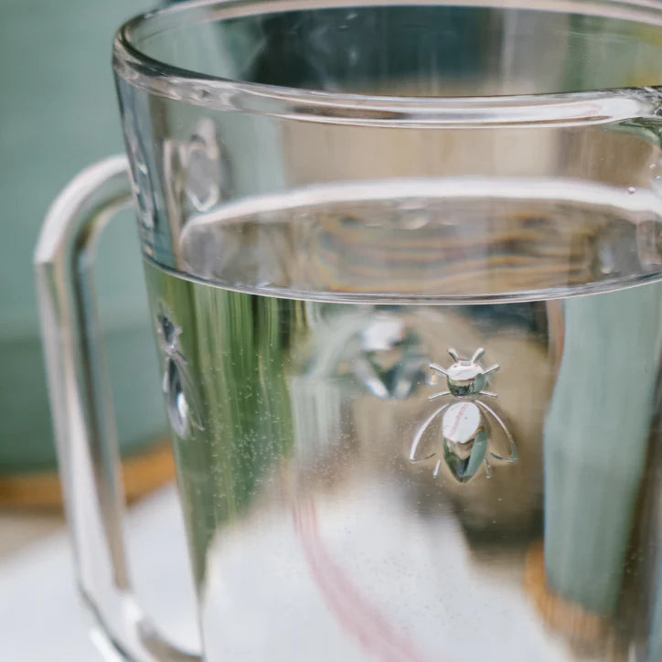 Clear glass mug filled with water featuring silver bee decorations on the surface