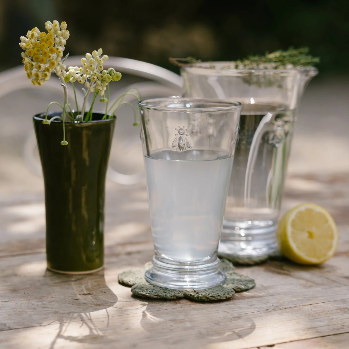 Clear glass of water with lemon juice, glass pitcher with water and lemon half on wooden table