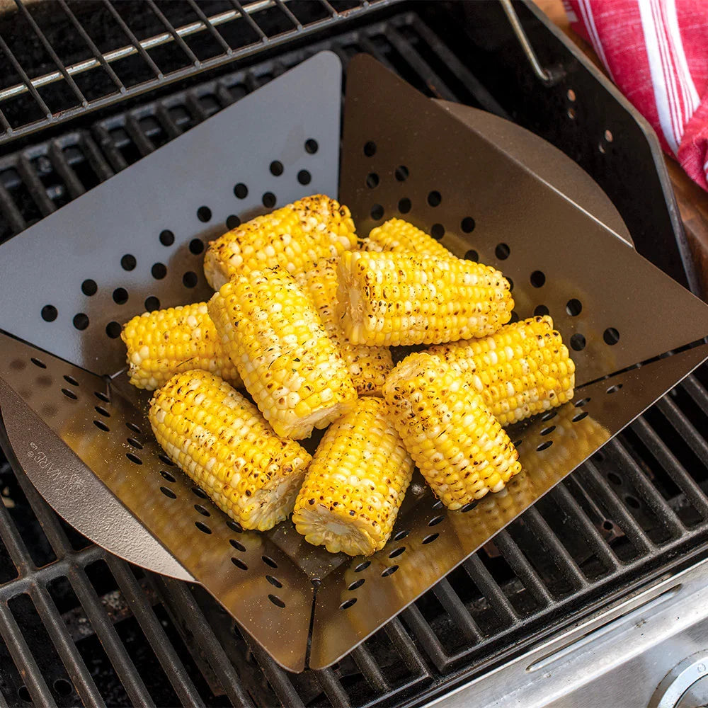Grilled corn pieces in a perforated grill basket on a barbecue grill