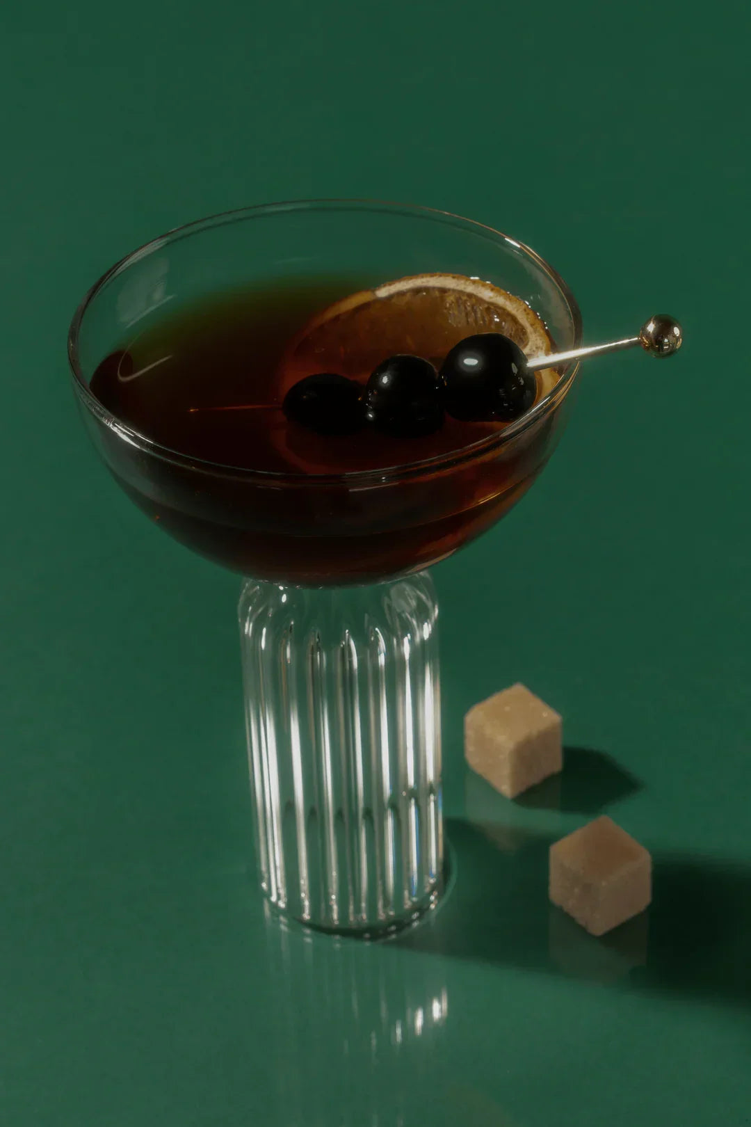 Elegant cocktail in a ribbed glass with lemon slice and black olives on green surface with sugar cubes