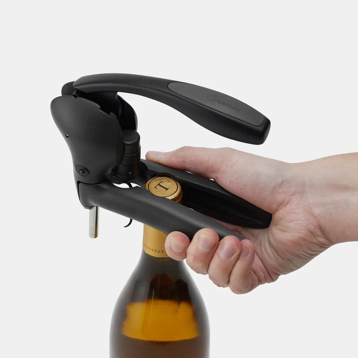 Hand using black lever corkscrew to open wine bottle with gold foil