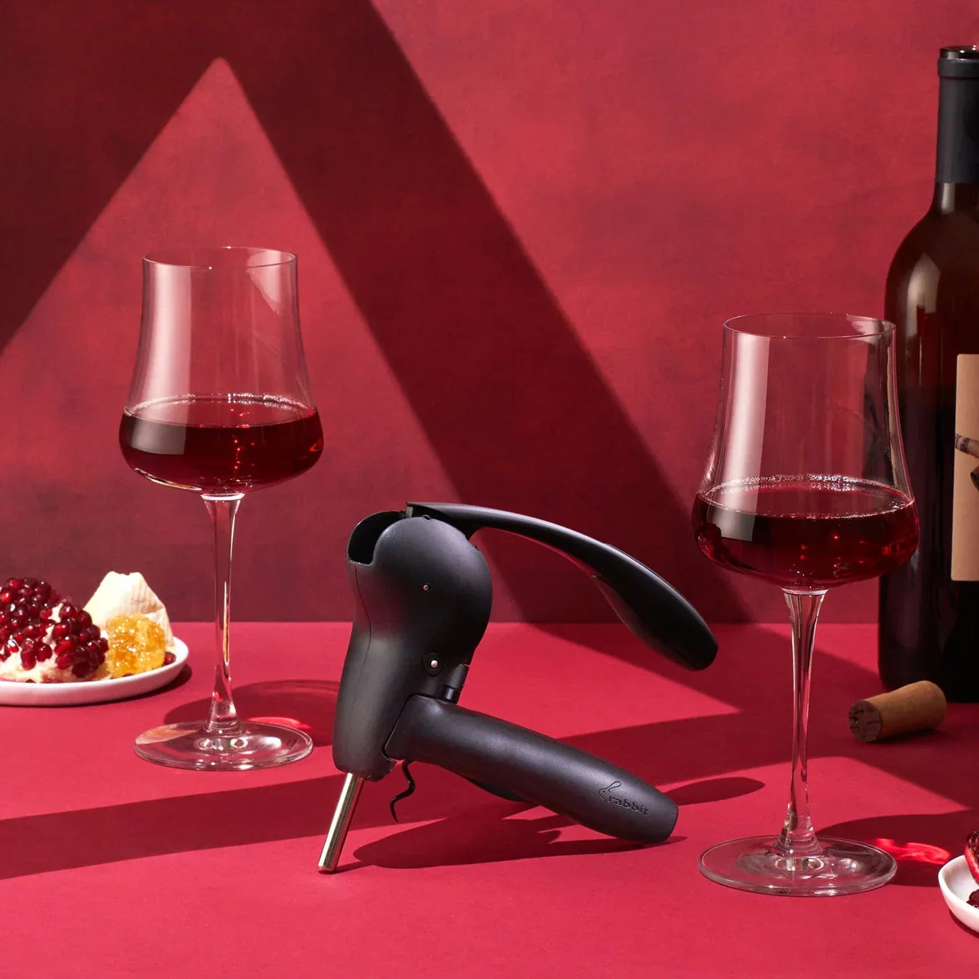 Black lever corkscrew opener with two glasses of red wine and wine bottle on red surface