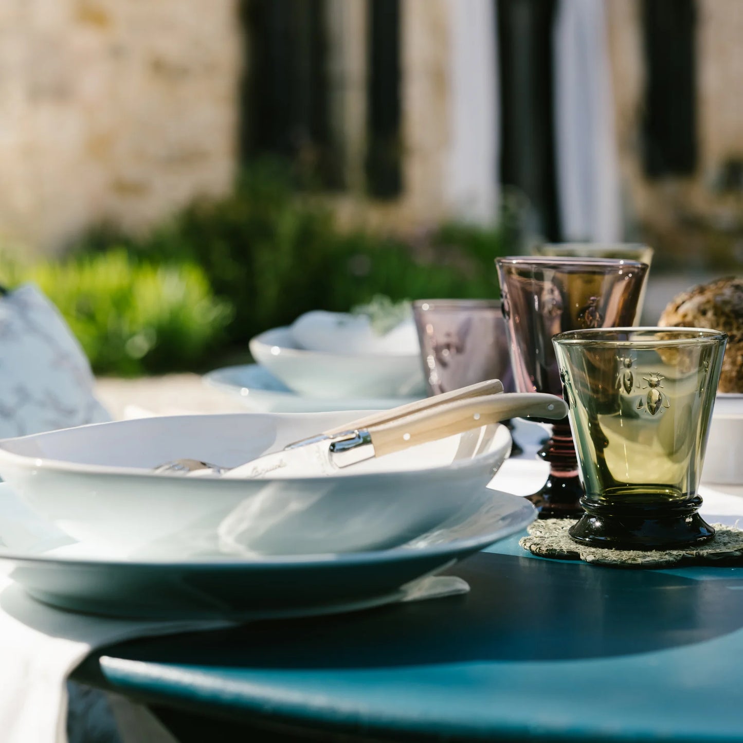 Outdoor table setting with white plates, ivory-handled cutlery, and colored embossed glass tumblers