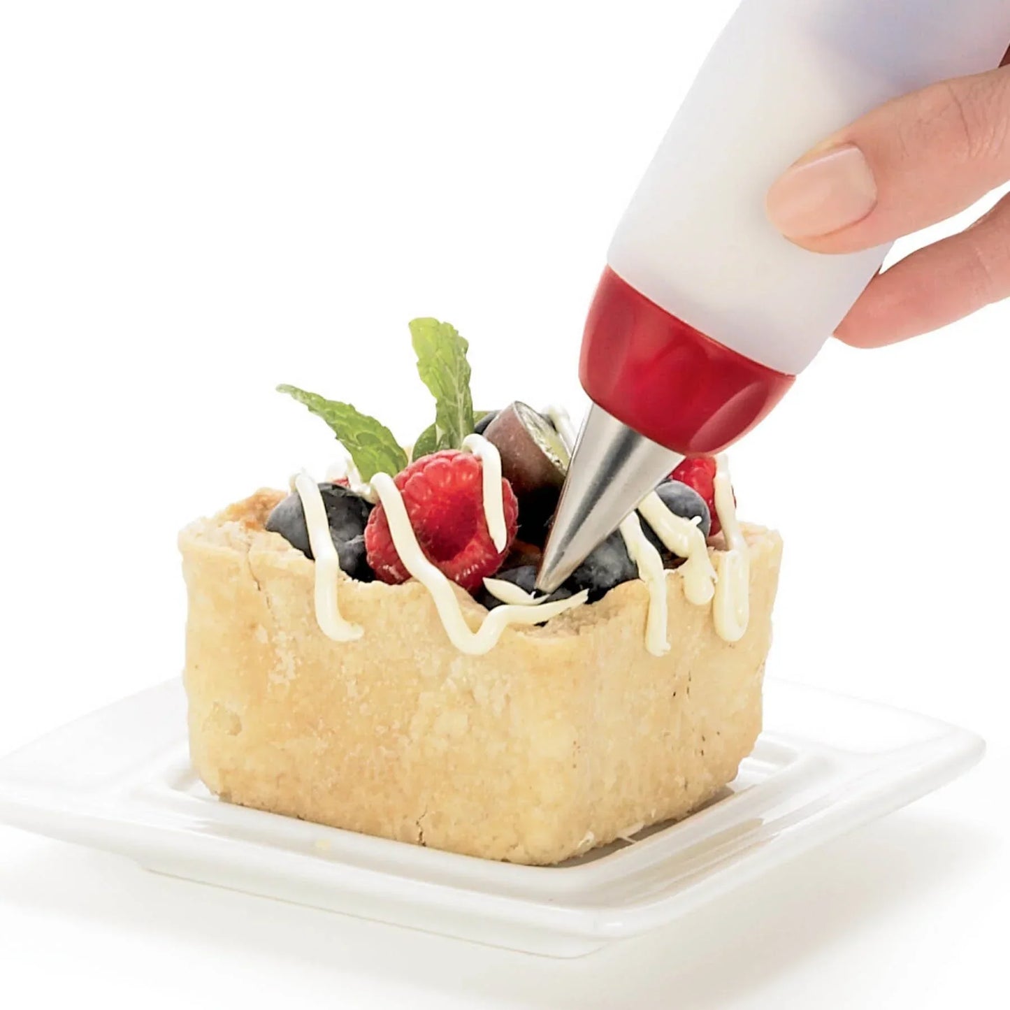 Hand decorating square fruit tart with white icing using a piping bag on white plate