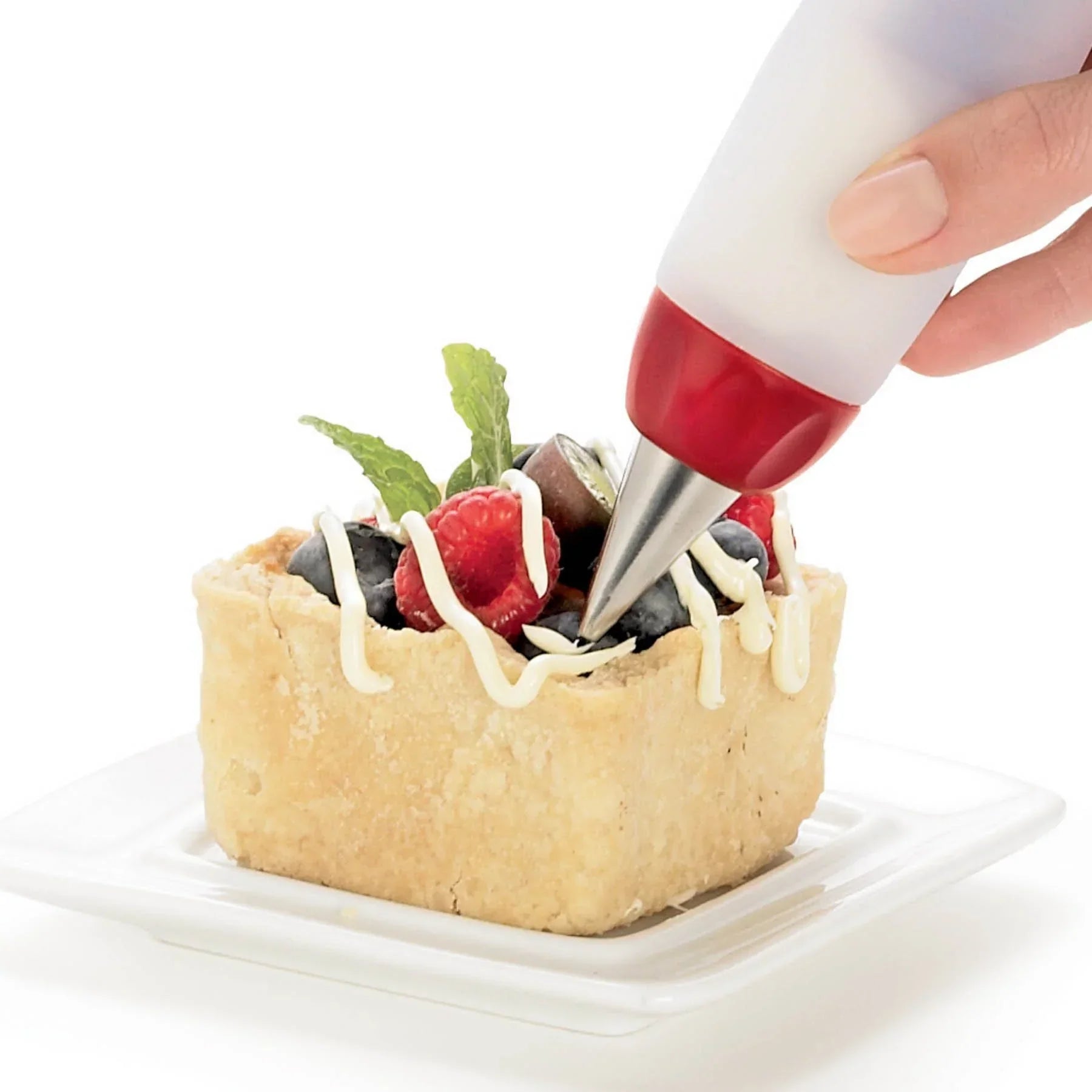Hand decorating square fruit tart with white icing using a piping bag on white plate