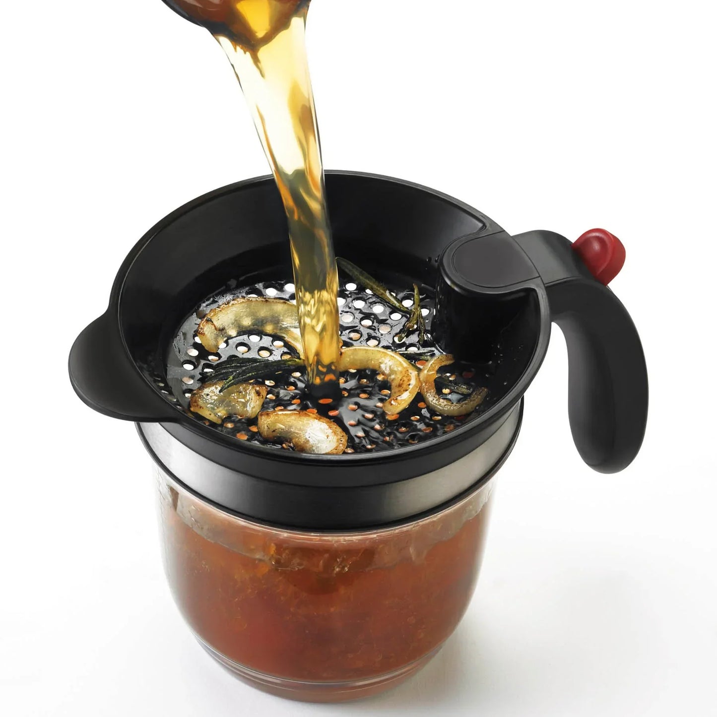 Black metal cocktail strainer with lemon and herbs straining brown liquid into glass jar